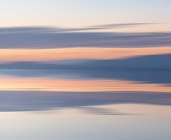 Epic sunset landscape image looking across the sea from Cumbria towards mountains of Dunfries and Galloway in Scotland with pastel colors reflected in the calm ocean