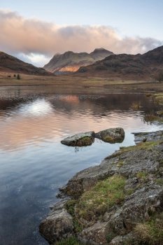 Epic landscape of sunrise light over Blea Tarn in Lake District with stunning light on distant mountains