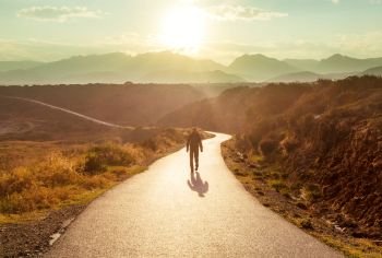 Scenic road in the mountains. Travel background. Man going on sunrise background.