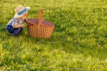 Portrait of toddler child outdoors. Rural scene with one year old baby boy wearing straw hat looking in picnic basket