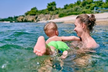 Two year old toddler boy learns to swim with mother 