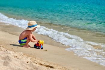 Two year old toddler boy on beach with toys. Kid wearing straw sun hat. Summer family vacation. Sithonia, Greece