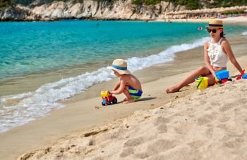 Two year old toddler boy on beach with mother playing with beach toy. Summer family vacation. Sithonia, Greece. 