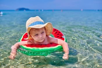 Two year old toddler boy on beach swimming with inflatable ring