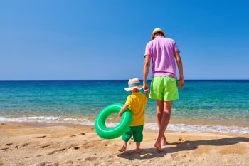 Two year old toddler boy walking on beach with father, holding inflatable ring. Summer family vacation. Sithonia, Greece. 