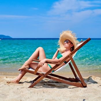 Woman in bikini on beach sitting in lounger chair, Sithonia, Greece