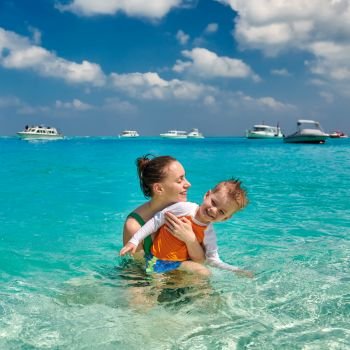 Three year old toddler boy on beach with mother having fun in shallow water. Summer family vacation at Maldives.