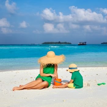 Family on beach, woman in green dress with three year old boy. Summer vacation at Maldives.