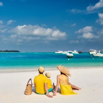 Family on beach, young couple in yellow with three year old boy. Summer vacation at Maldives.