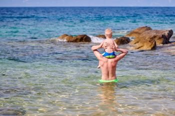 Two year old toddler boy on father’s shoulders at beach