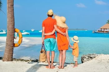 Family on beach, young couple in orange with three year old boy under the palm tree. Summer vacation at Maldives.