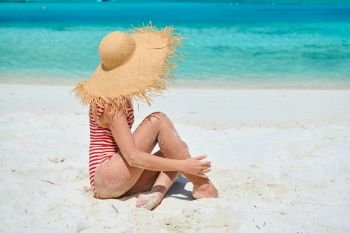 Woman in one-piece swimsuit at tropical beach with white sand. Summer vacation at Maldives.
