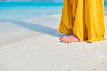 Woman legs in yellow dress on tropical beach. Summer vacation at Maldives.