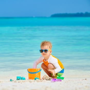 Three year old toddler boy playing with beach toys on beach.  Summer family vacation at Maldives.