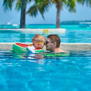 Three year old toddler boy in resort swimming pool eskimo kissing his father. Summer family vacation at Maldives.
