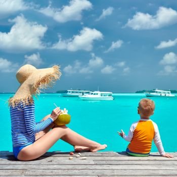 Three year old toddler boy with mother sitting on wooden jetty. Summer family vacation at Maldives.