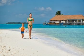 Three year old toddler boy running on beach with mother. Summer family vacation at Maldives.