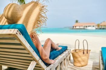 Young woman at beach on wooden sun bed loungers. Summer vacation at Maldives.