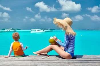 Three year old toddler boy with mother sitting on wooden jetty. Summer family vacation at Maldives.