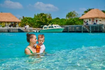 Three year old toddler boy on beach with mother having fun in shallow water. Summer family vacation at Maldives.