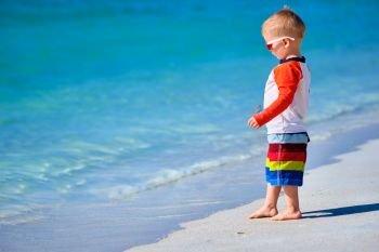 Two year old toddler boy in sunglasses walking on beach 