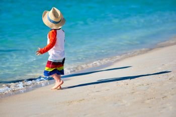 Two year old toddler boy in sun hat walking on beach 