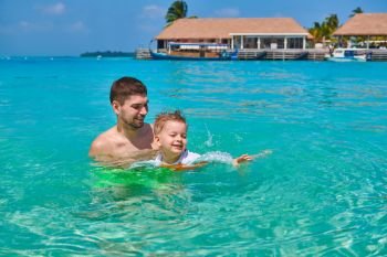 Three year old toddler boy learns to swim with father. Summer family vacation at Maldives.