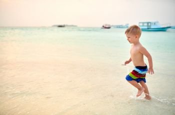 Three year old toddler boy on beach at sunset. Summer family vacation at Maldives.