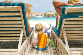 Family at beach on wooden sun bed loungers, young couple with three year old boy. Summer vacation at Maldives.