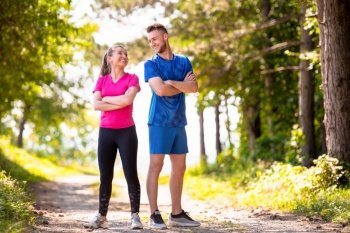 portrait of young happy couple enjoying in a healthy lifestyle while jogging on a country road through the beautiful sunny forest, exercise and fitness concept