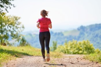 woman enjoying in a healthy lifestyle while jogging on a country road through the beautiful sunny forest, exercise and fitness concept