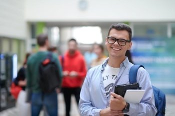 a student in glasses stands in the hallway of a modern college and uses a laptop
