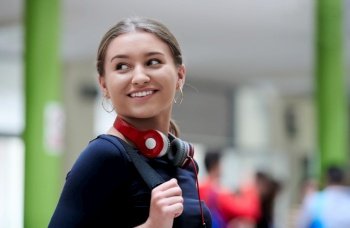 portrait of a happy young student getting ready for class while waiting in the college hallway with headphones and laptop