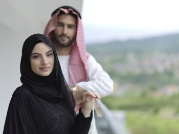 portrait of young arabian muslim couple in traditional clothes standing on balcony representing modern islam fashion and ramadan kareem concept