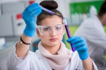 young female student with protective glasses making chemistry experiment in bright laboratory,education and medicine concept