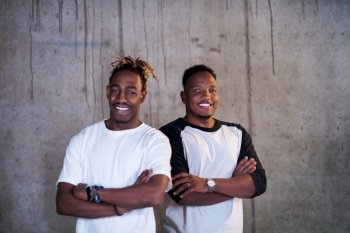 portrait of two young african american smiling casual businessmen standing in front of a concrete wall at new startup office