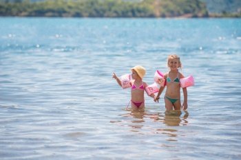 two happy little girls with swimming armbands playing in shallow water of the sea during Summer vacation  Healthy childhood lifestyle concept