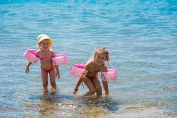 two happy little girls with swimming armbands playing in shallow water of the sea during Summer vacation  Healthy childhood lifestyle concept
