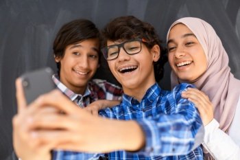 Group of Arab teens taking selfie photos on a smartphone with a black chalkboard in the background. Selective focus. High quality photo. Group of arab teens taking selfie photo on smart phone with black chalkboard in background. Selective focus 