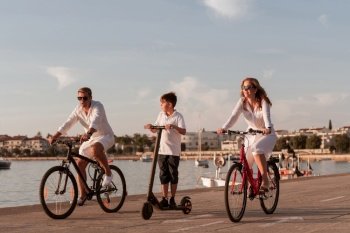 Happy family enjoying a beautiful morning by the sea together, parents riding a bike and their son riding an electric scooter. Selective focus. High-quality photo. Happy family enjoying a beautiful morning by the sea together, parents riding a bike and their son riding an electric scooter. Selective focus 