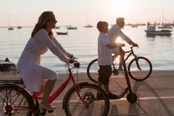 Happy family enjoying a beautiful morning by the sea together, parents riding a bike and their son riding an electric scooter. Selective focus. High-quality photo. Happy family enjoying a beautiful morning by the sea together, parents riding a bike and their son riding an electric scooter. Selective focus 