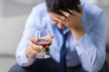 alcoholism, alcohol addiction and people concept - male alcoholic drinking brandy at home. drunk man with glass of alcohol at home