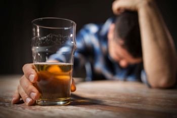alcoholism, alcohol addiction and people concept - male alcoholic with glass of beer lying or sleeping on table at night. drunk man with glass of alcohol on table at night