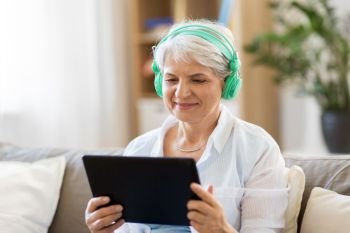 technology, people and lifestyle concept - happy senior woman in headphones and tablet pc computer listening to music at home. senior woman in headphones listening to music