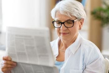 age and people concept - portrait of senior woman reading newspaper at home. portrait of senior woman reading newspaper at home