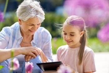 family, leisure and technology concept - happy grandmother and granddaughter with tablet pc computer at summer garden. grandmother and girl with tablet pc at garden