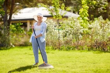 gardening and people concept - happy senior woman with lawn rake working at summer garden. senior woman with lawn rake working at garden