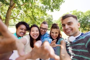 people, friendship and international concept - happy smiling young woman and group of happy friends taking selfie outdoors. group of happy international friends taking selfie