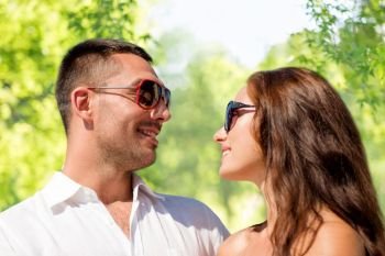 love, summer and relationships concept - happy smiling couple in sunglasses over green natural background. happy couple in sunglasses over green background