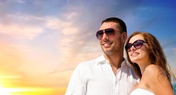 love, summer and relationships concept - happy smiling couple in sunglasses over evening sky background. happy smiling couple in sunglasses